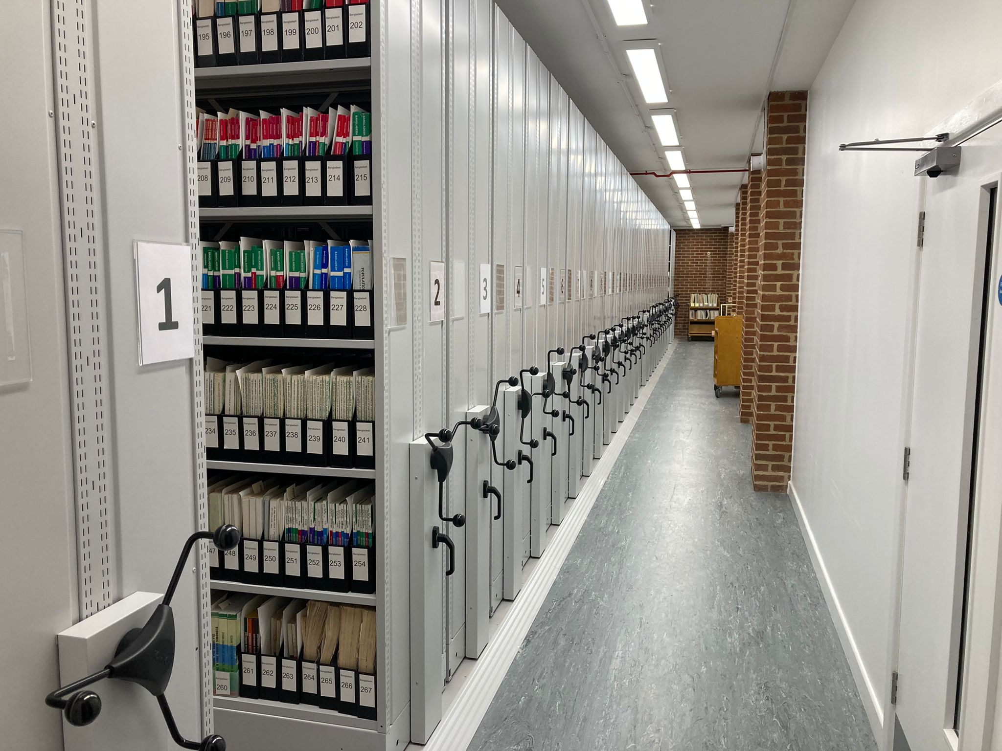 New roller-racking - grey metal shelving, with pamphlet boxes stored on them. Painted white walls and grey laminate flooring